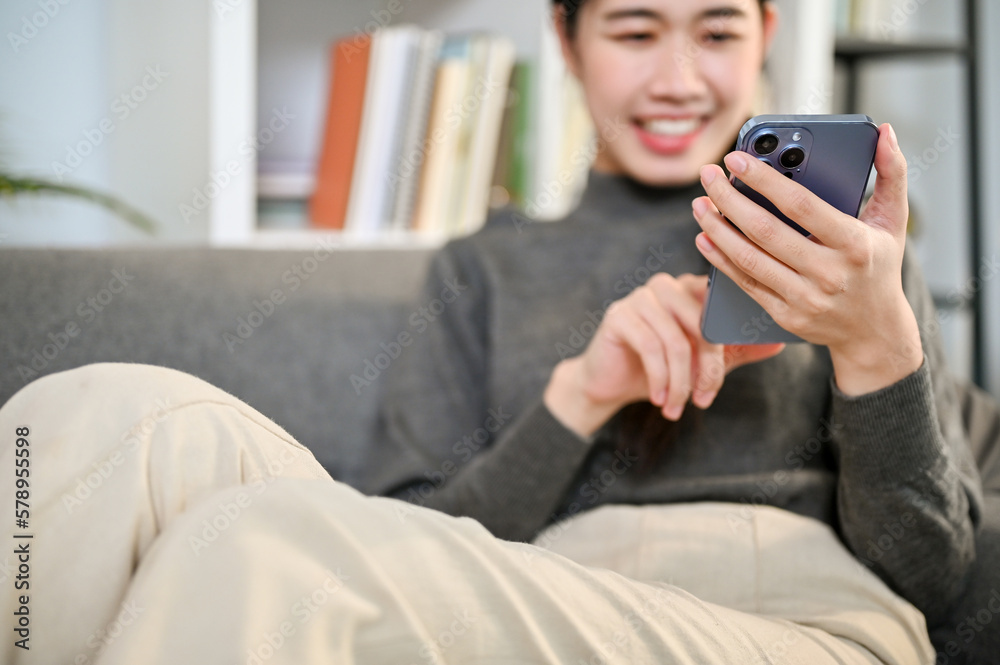 Cropped image, Charming Asian woman using her phone while relaxing on sofa in living room. Cropped image, Charming Asian woman using her phone while relaxing on sofa in living room.