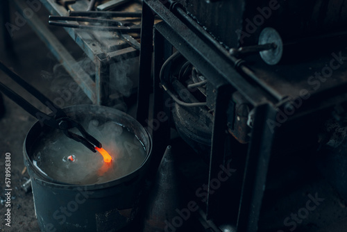 Blacksmith forges and tempering metal horseshoe in jar with water at forge. photo