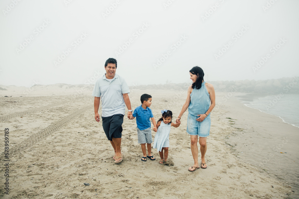 Family Of Four Walking Along The Water At Foggy Beach Family Of Four Walking Along The Water At Foggy Beach
