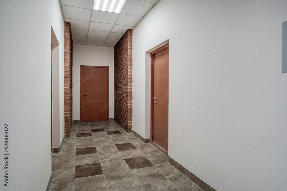 white empty long corridor with red brick walls and doors in interior of modern apartments or office