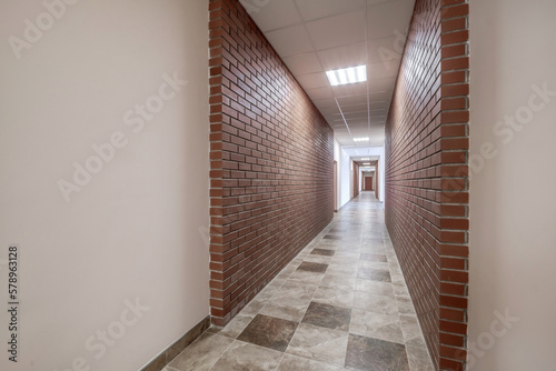 white empty long corridor with red brick walls and doors in interior of modern apartments or office