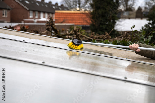 Washing the patio pergola roof cover made of aluminum. removing the dirty algae with brush soap and water close up in garden from a house terrace