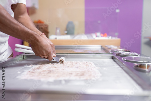 A worker is using a spatula to roll an ice cream on a freeze machine