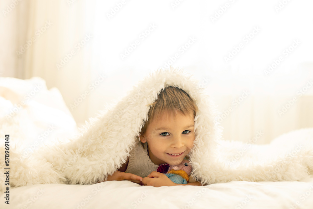 Little toddler child, cute kid with knitted small cute animal toy, lying in bed