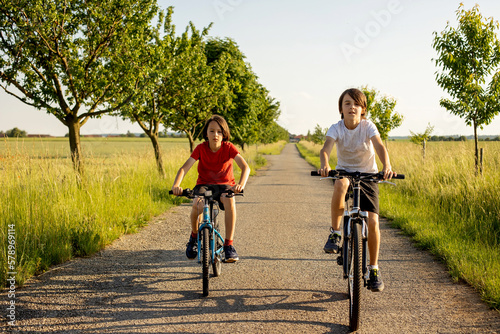 Cute happy children, brothers, riding bikes in the park on a sunny summer day