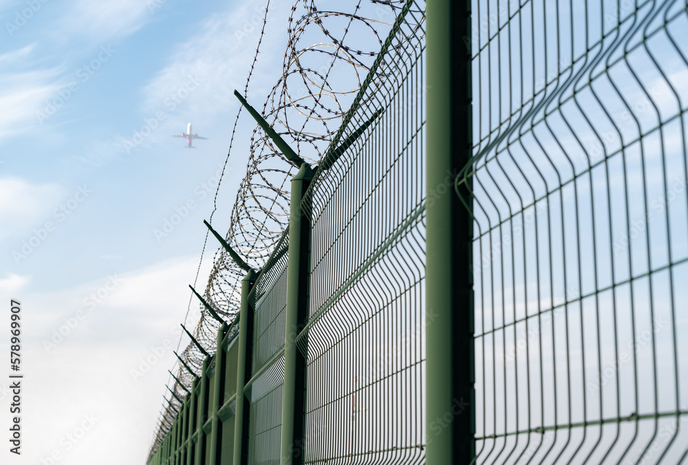 Barbed wire fence detail. Blurred airplane in the background.