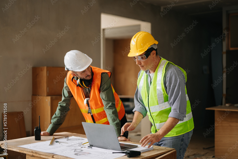 Contractor and architect looking at plan, tablet, laptop and talking about working on big project. Building in construction process interior. team work . Contractor and architect looking at plan, tablet, laptop and talking about working on big project. Building in construction process interior. team work .