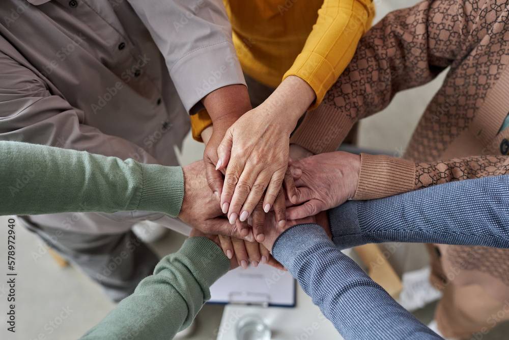 Top view closeup of senior people stacking hands in circle during support group session in retirement home