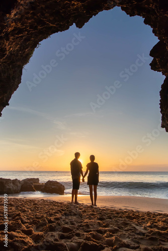 Photo of a couple at Tegal Wangi Beach, Jimbaran, Bali taken from inside the cave while sunset. People are outside the cave on the beach at afternoon. photo