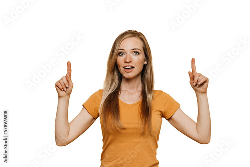 Redhead young adult woman in orange t-shirt pointing up  at empty space by index fingers against transparent background. Cheerful caucasian girl toothy smiles. Mockup, promo, sale, discount.