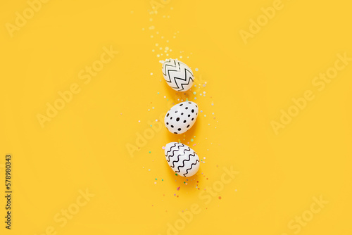 Photography white Easter eggs with stripes and a dot with confetti on a bright yellow background