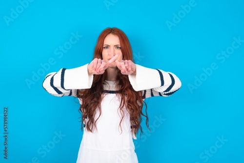 young caucasian woman wearing overalls over blue background has rejection angry expression crossing fingers doing negative sign. photo