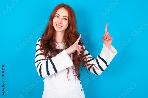 Positive young caucasian woman wearing overalls over blue background with beaming smile pointing with two fingers and looking on empty copy space. Advertisement concept.