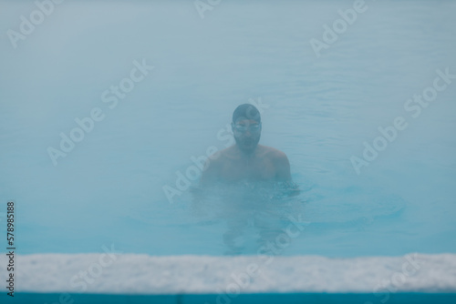 Fit swimmer male training swim in open winter swimming pool with fog. Geothermal outdoor spa health concept.