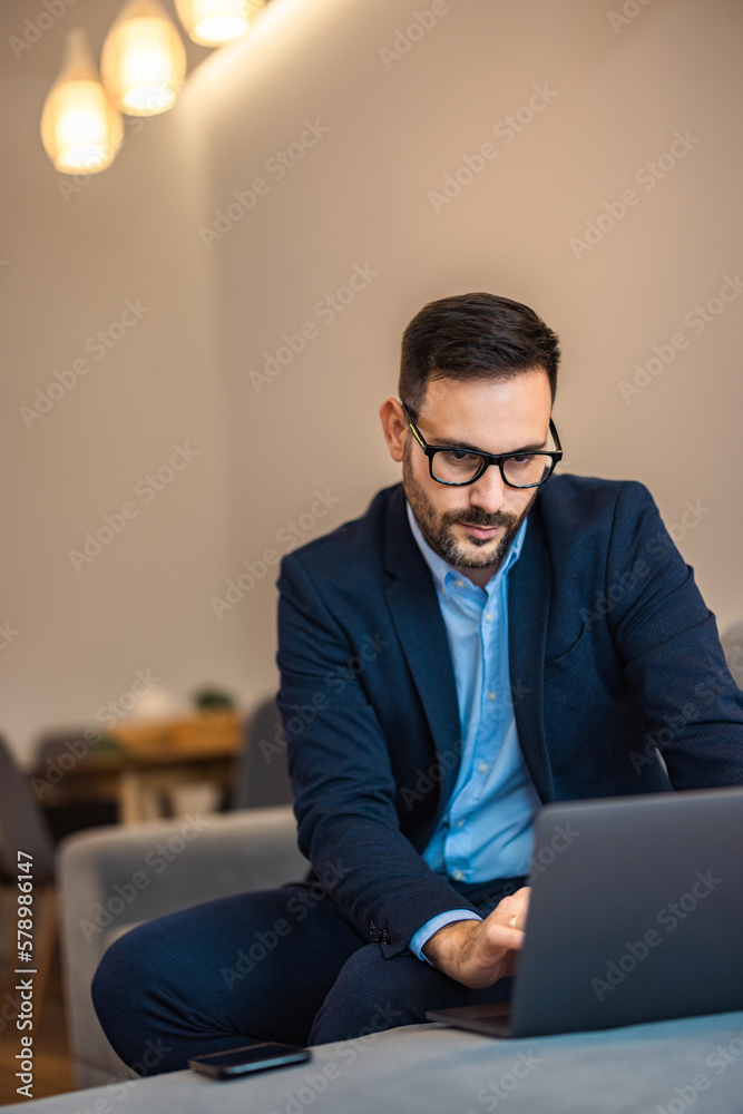 Focused businessman working over the laptop, sitting on the couch in the living room. Focused businessman working over the laptop, sitting on the couch in the living room.
