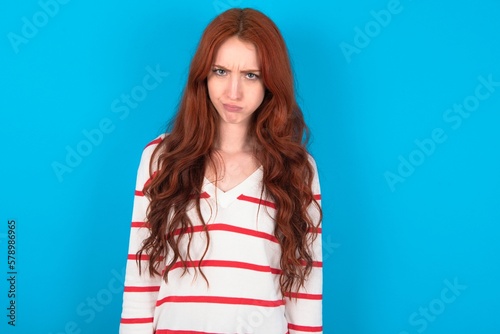 Bilde på lerret Offended dissatisfied young woman wearing striped sweater over blue background w