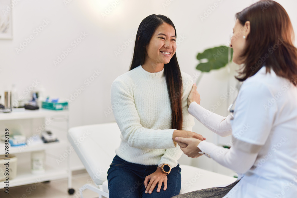 Fototapeta premium A smiling Asian woman patient sitting with a female doctor in the examination room.
