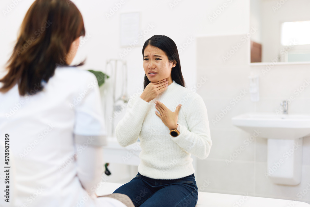 The female Asian patient complains of a sore throat, talking with a female doctor at the office. The female Asian patient complains of a sore throat, talking with a female doctor at the office.