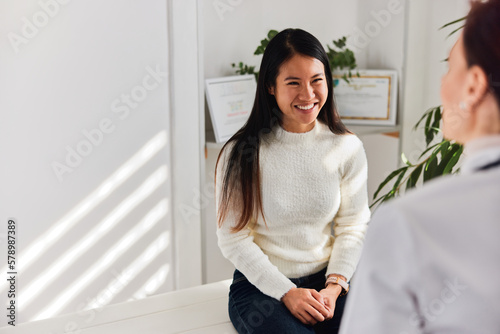 A smiling Asian female patient talking with a female doctor at the clinic.