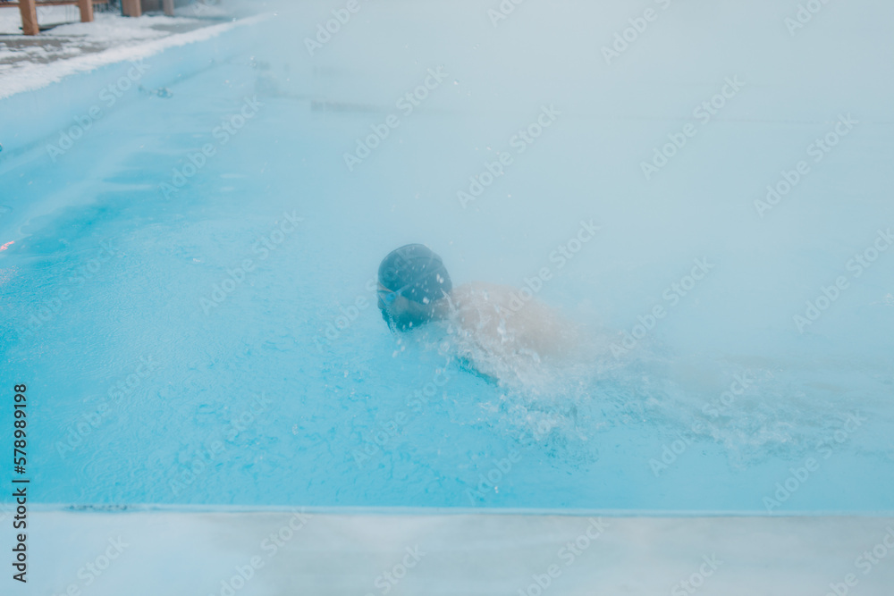 Fit swimmer male training swim butterfly stroke in open winter swimming pool with fog. Geothermal outdoor spa health concept.