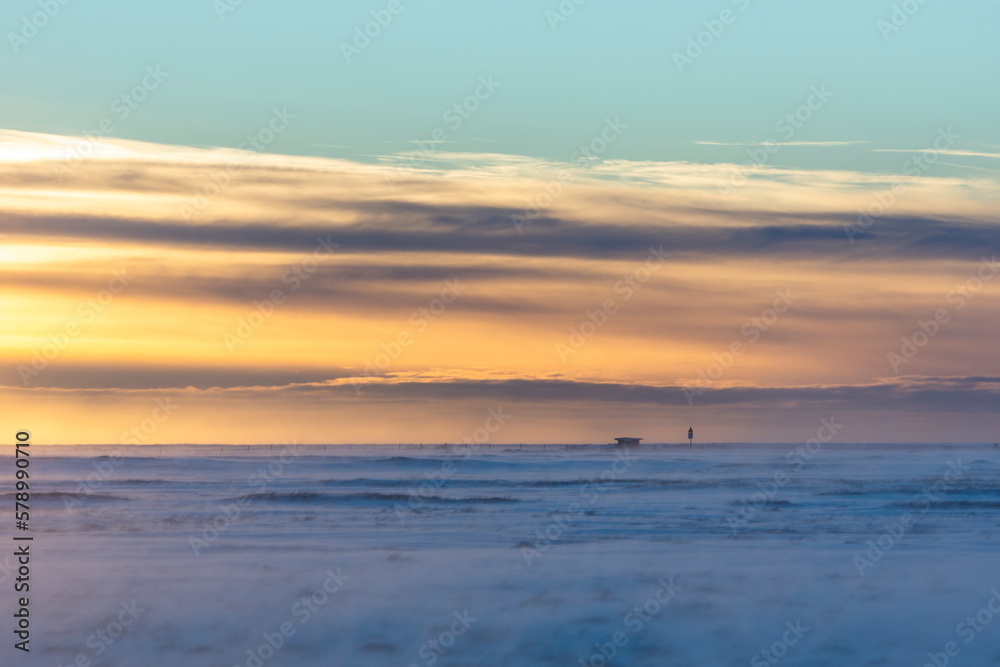 imagen de un paisaje nevado con el cielo lleno de nubes coloreadas por el sol y el cielo azul 
