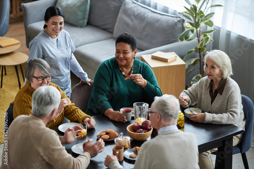 High angle view at group of senior people sitting at table together and smiling happily in retirement home