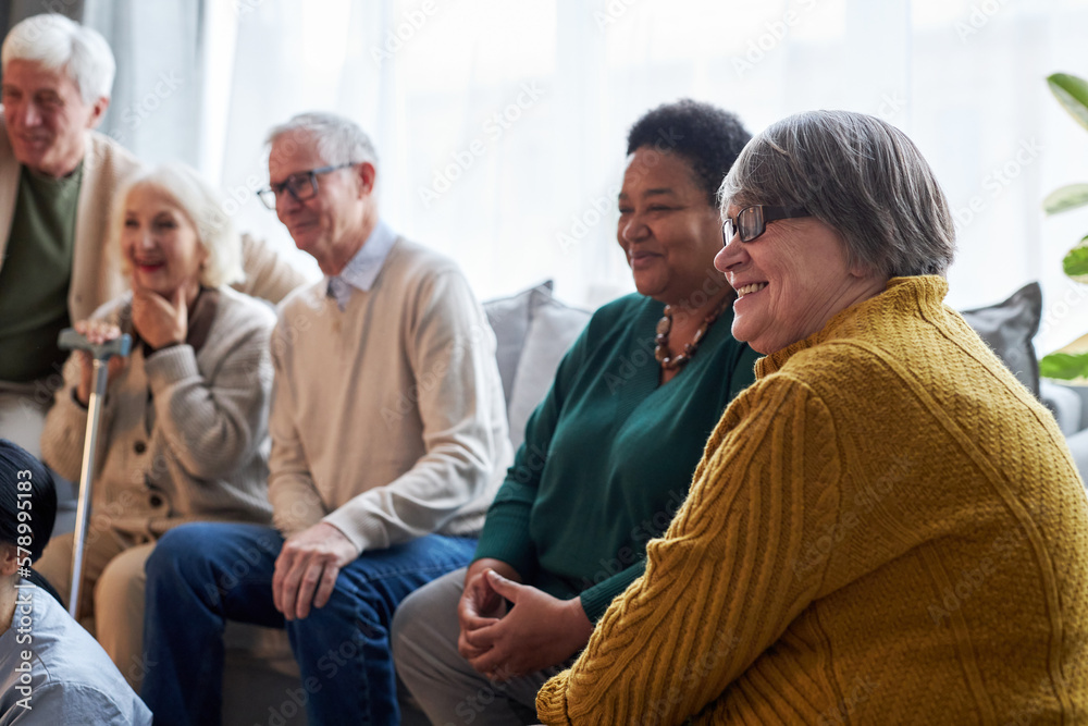 Side view at group of smiling senior people watching TV while sitting in row in retirement home facility Side view at group of smiling senior people watching TV while sitting in row in retirement home facility