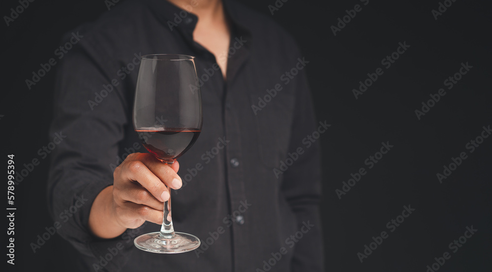 Close-up of hand holding a red wine glass while standing on a black background