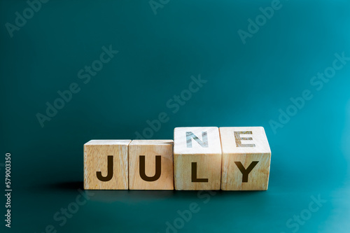 Changing the month of mid of the year. Flipping wooden cube blocks for change words, months from June to July, isolated on blue background with copy space, clean, modern, and minimal style. photo