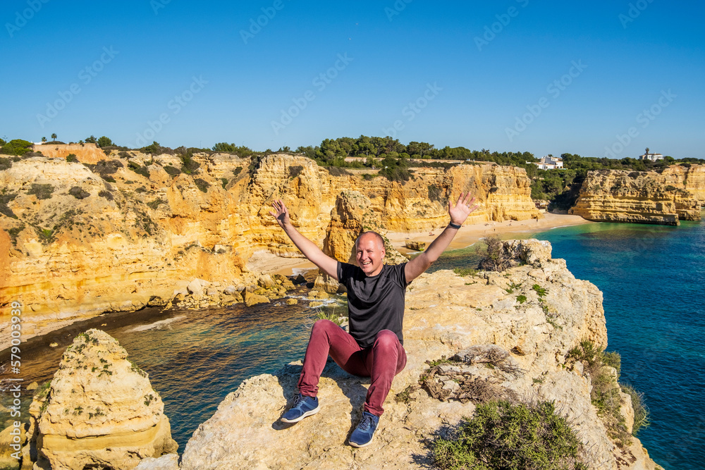 Naklejka premium Happy man sitting on the top of cliffs at Marinha beach, Algarve, Portugal