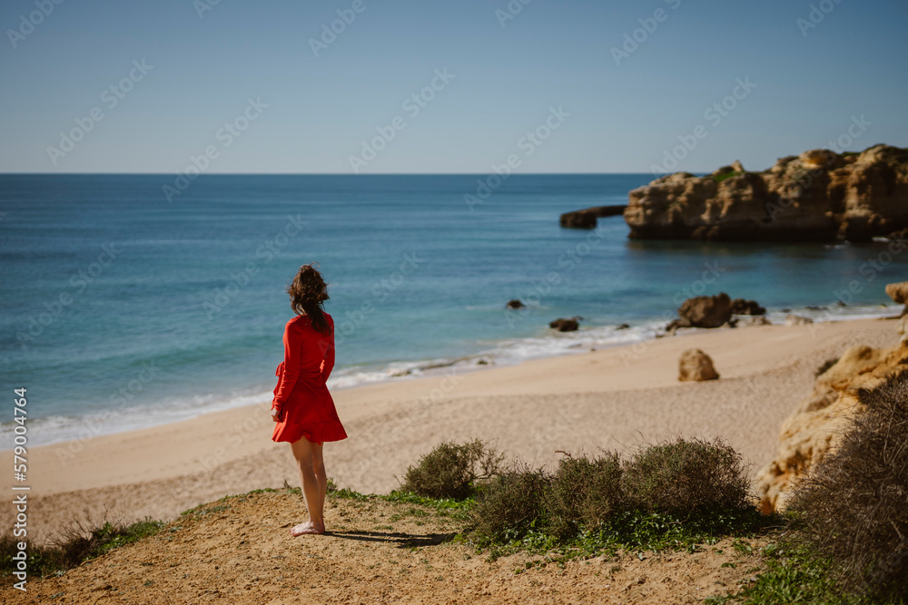 Attractive woman in red dress on top of cliffs at Sao Rafael Beach, Algarve, south Portugal