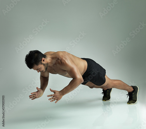 Hes fighting fit. Studio shot of a young man doing a clap pushup against a gray background.