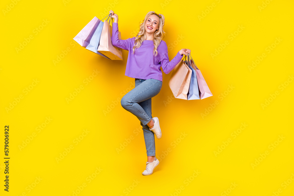 Full size photo of pretty young girl holding shopping bags packages dressed stylish violet clothes isolated on yellow color background Full size photo of pretty young girl holding shopping bags packages dressed stylish violet clothes isolated on yellow color background