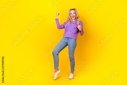 Full body photo of attractive young woman raise fists luck win lottery dressed stylish violet outfit isolated on yellow color background © deagreez