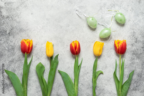Tulips and decorative Easter eggs on a gray background. Top view, flat lay.
