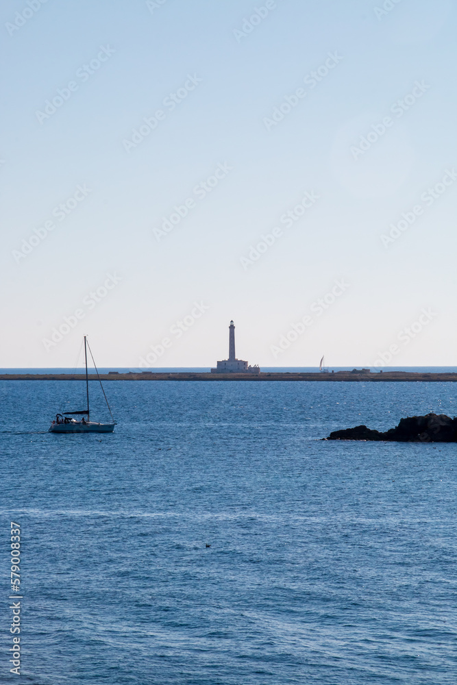 Faro de la isla de Sant' Andrea desde el casco antiguo de Gallipoli, Italia. Paisaje a contra luz con un velero navegando junto al faro y las otras islas.