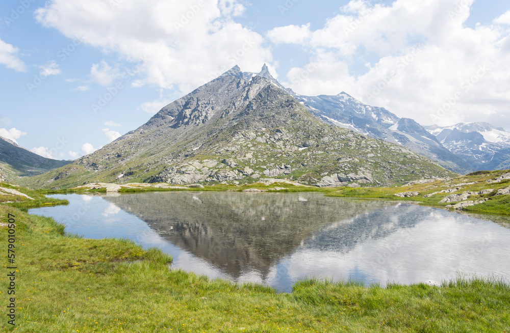 Green mountain landscape in summer with a reflection of the mountain in the lake, the sky is blue with soft clouds. This was a hike in the Alps to Mount Cenis Lake