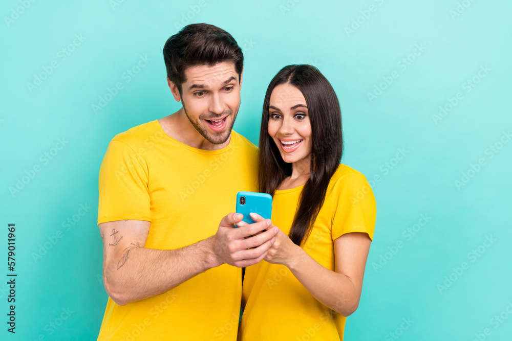 Naklejka premium Photo of surprised lovely couple hold smartphone wear yellow t-shirts enjoy crazy black friday sale website isolated on aquamarine color background