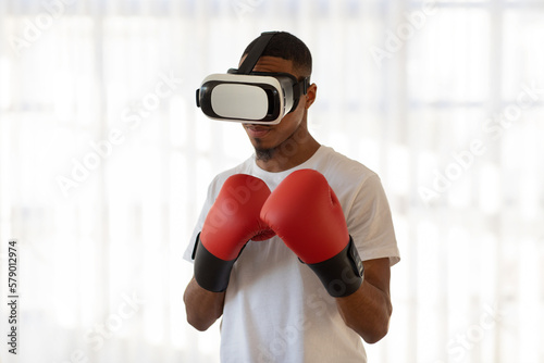 Athletic young black man in VR glasses and boxing gloves