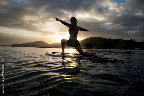 Woman with open arms over stand Up paddle at sunrise, Brazilian beach