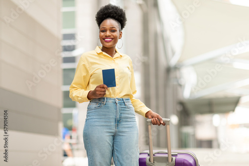 Happy Black Woman With Suitcase Holding Passport At Airport