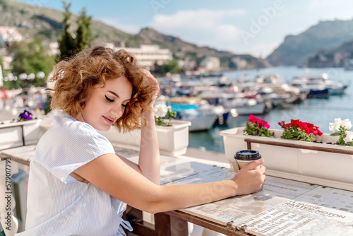 Happy beautiful woman drinking coffee with milk and having healthy breakfast in outdoor cafe in summer city in Europe.