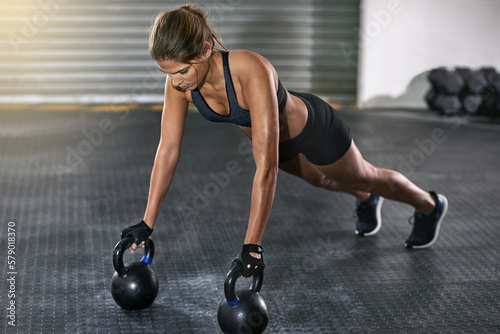 Fototapeta Naklejka Na Ścianę i Meble -  She trains like a beast. Full length shot of a young woman working out with kettle bells at the gym.