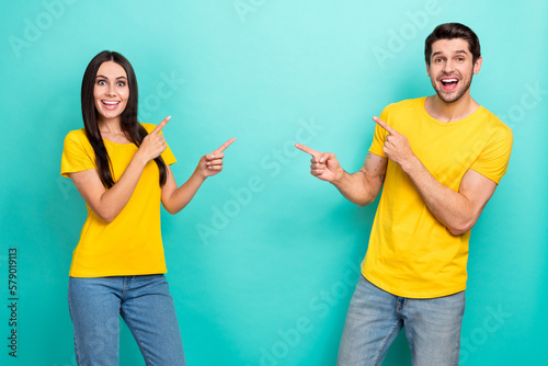 Photo of cheerful impressed married couple wear yellow t-shirts pointing fingers empty space isolated teal color background