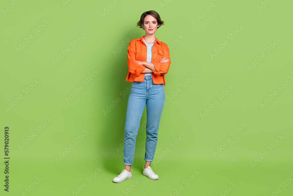 Full length photo of charming sweet lady dressed jeans shirt arms folded smiling isolated green color background Full length photo of charming sweet lady dressed jeans shirt arms folded smiling isolated green color background