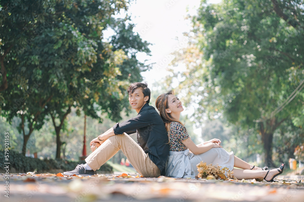 Fototapeta premium a couple sitting leaning against each other while enjoying the fallen leaves in the park