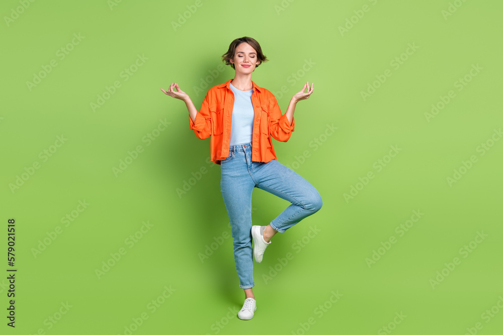 Full length photo of shiny dreamy lady dressed jeans shirt closed eyes enjoying yoga isolated green color background Full length photo of shiny dreamy lady dressed jeans shirt closed eyes enjoying yoga isolated green color background