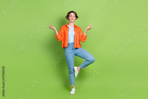 Full length photo of shiny dreamy lady dressed jeans shirt closed eyes enjoying yoga isolated green color background