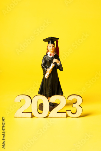 Class of 2023 concept. Wooden number 2023 with graduate statuette on color background photo