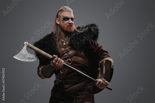 Shot of redhead scandinavian barbarian holding axe dressed in leather armor and fur.